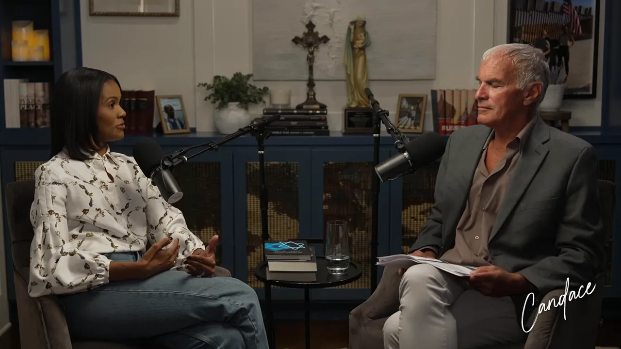 Wide two-shot of a podcast interview showing both participants, microphones, a book and notes on a small table between them.
