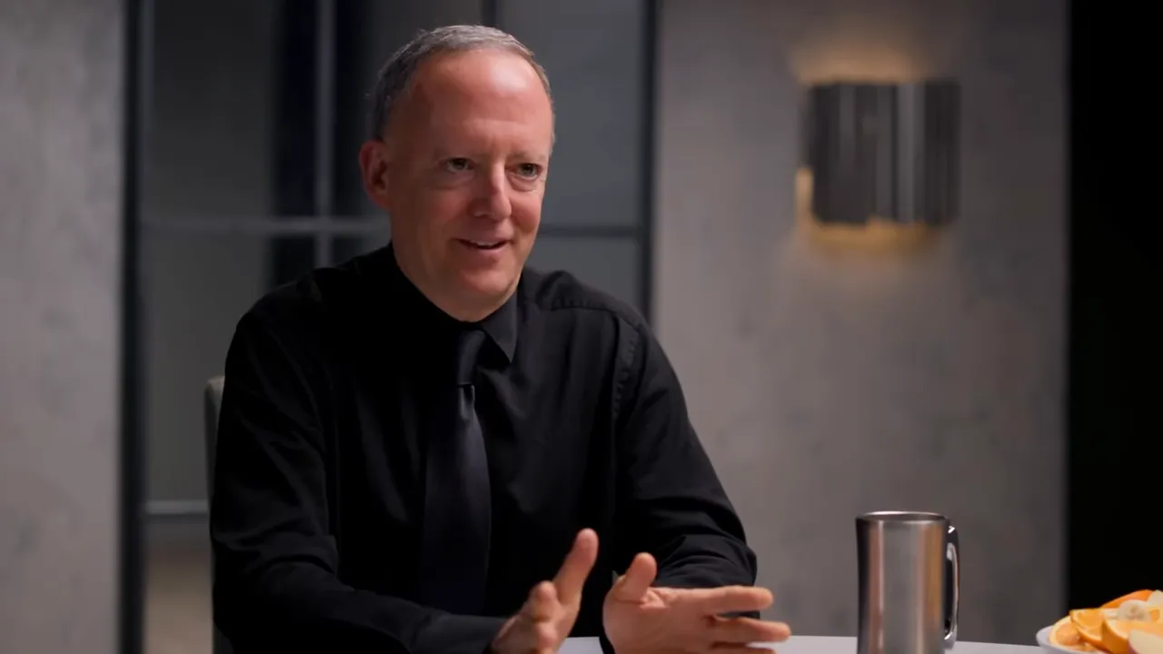 Interview guest smiling and gesturing while seated at table with mug and plate of fruit