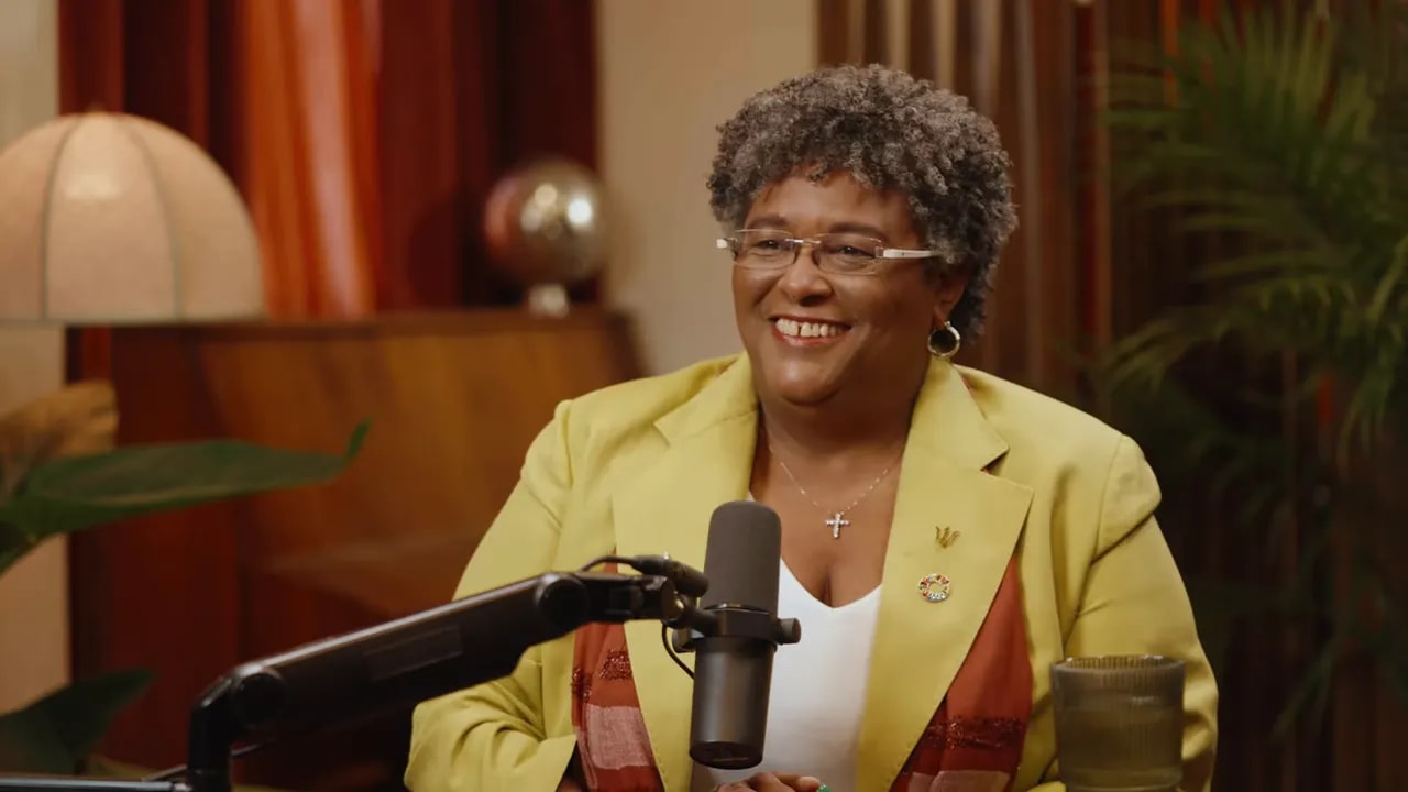 Smiling woman in a yellow blazer speaking into a podcast microphone in a warmly lit studio