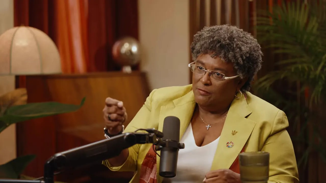 Woman in yellow blazer gesturing with hand while speaking into a podcast microphone