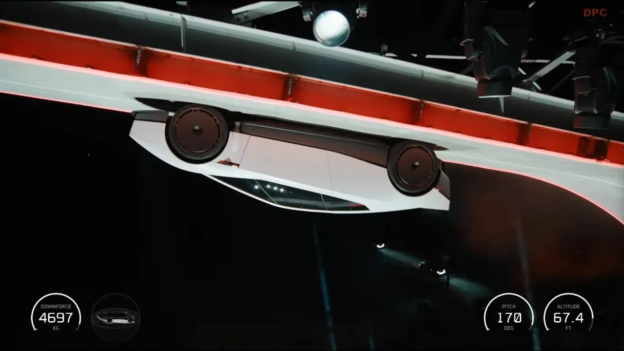White sports car positioned upside down beneath a curved ramp